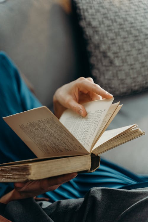 Person Sitting on Couch Reading Book 