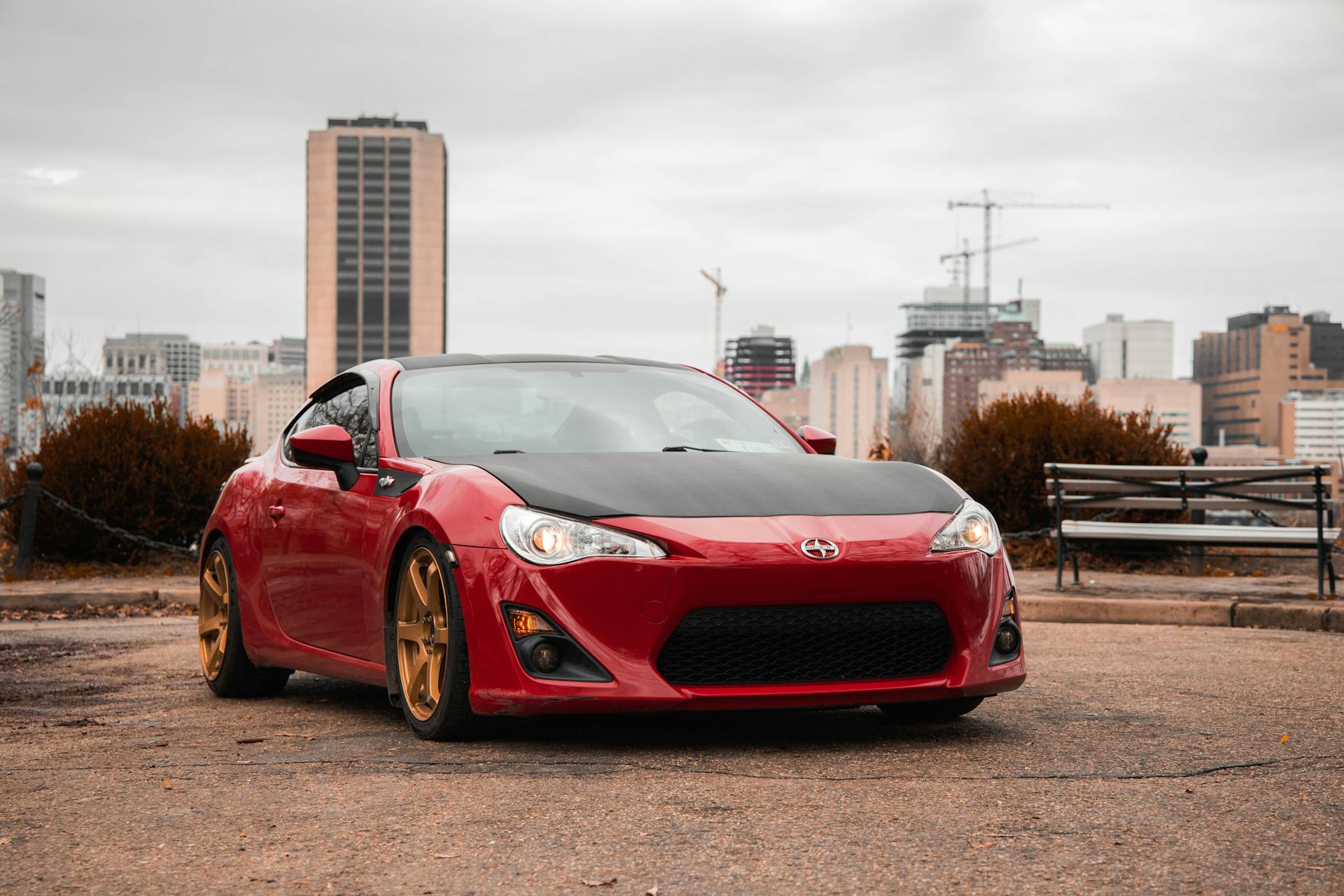 A sleek red sports car, 2013 Scion FR-S, parked with city skyline backdrop.