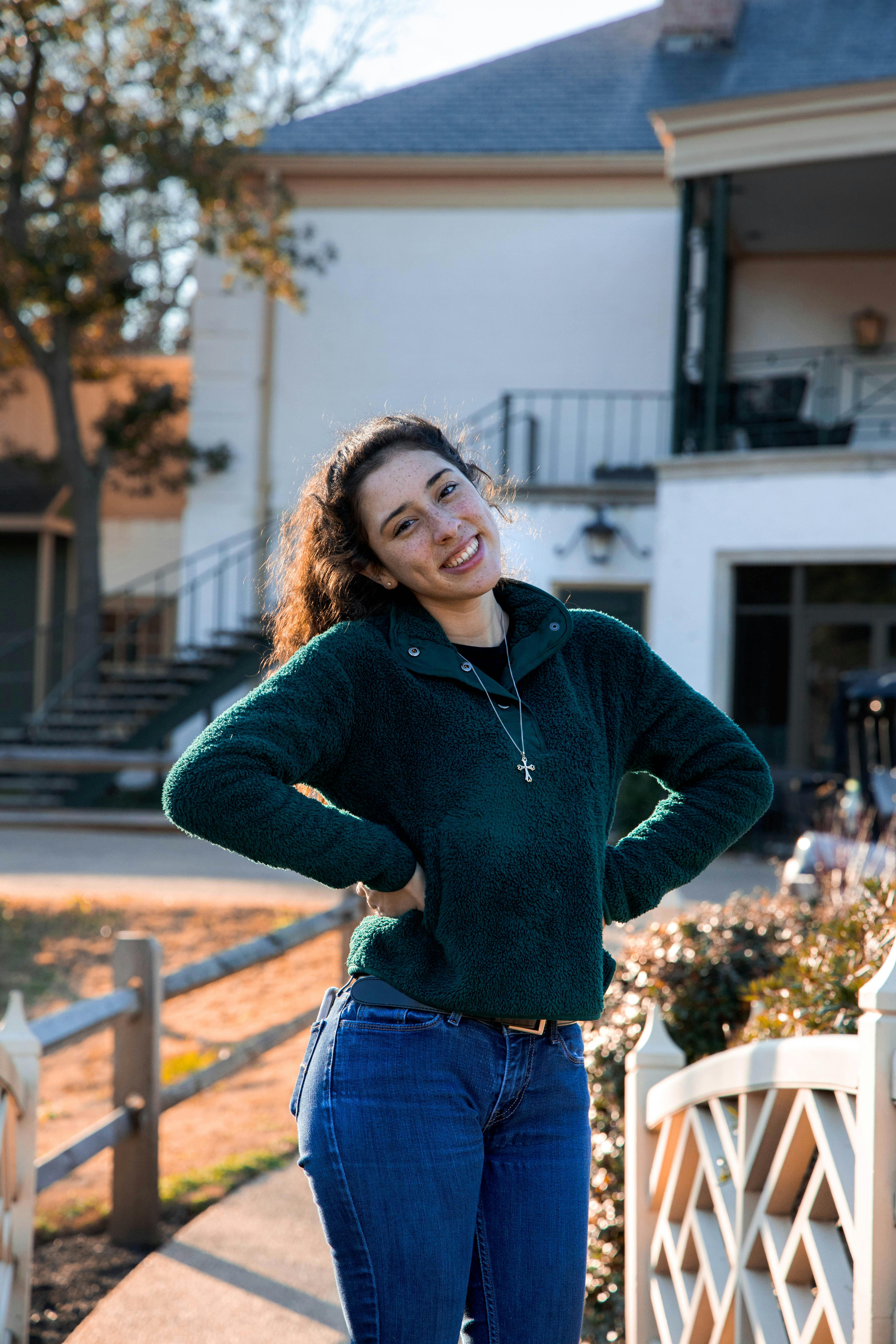 Bright portrait of a woman in a green jacket smiling outdoors during the fall season.