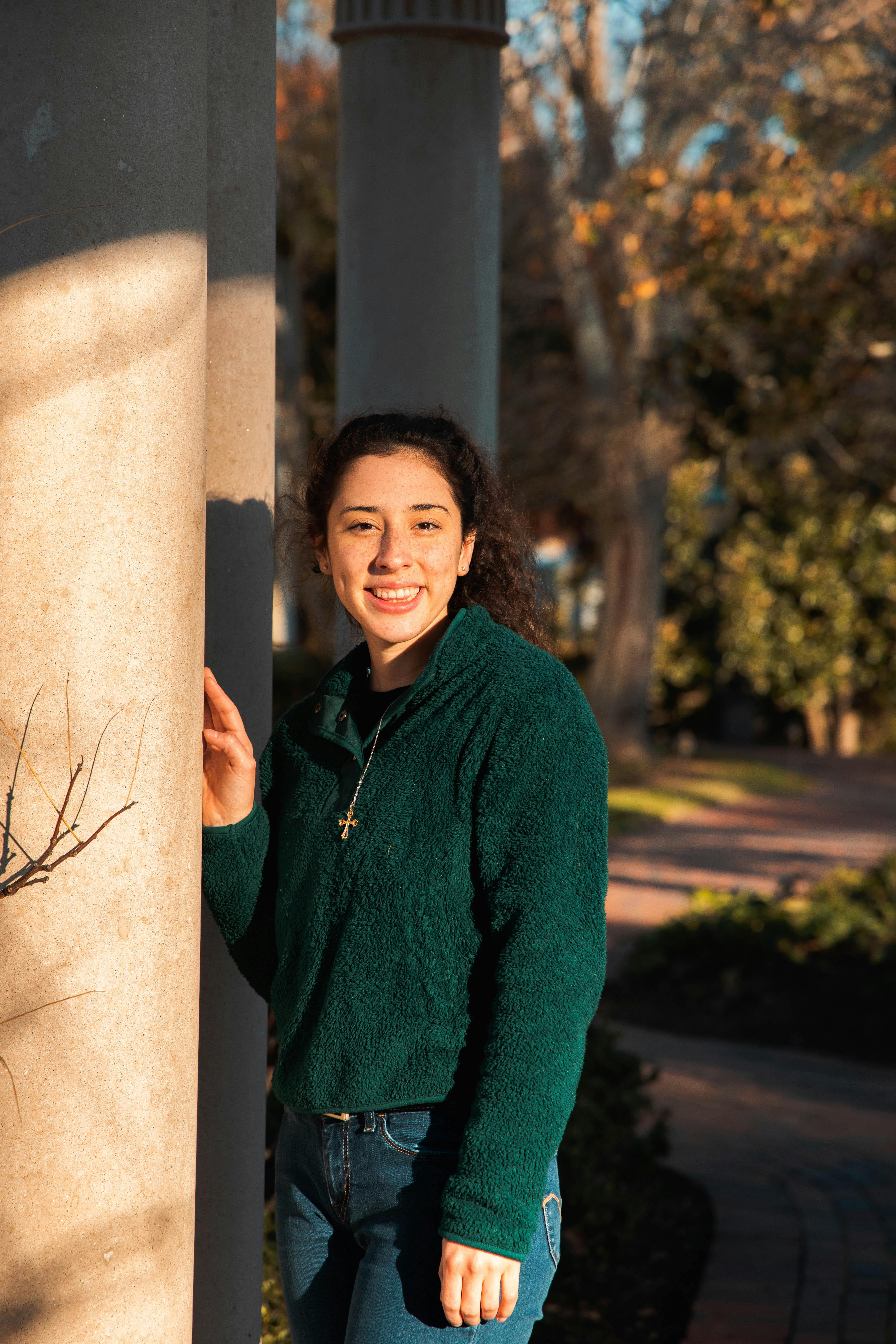 Smiling young woman in green sweater and jeans, standing outdoors.