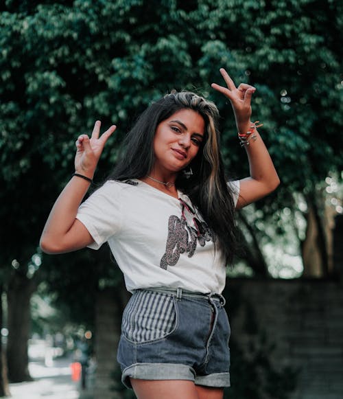 A Woman in a White Shirt and Denim Shorts Making Peace Signs