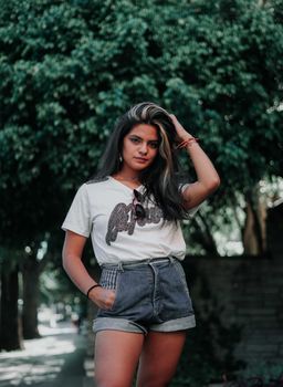 Fashionable young woman in denim shorts and white shirt posing confidently outdoors.