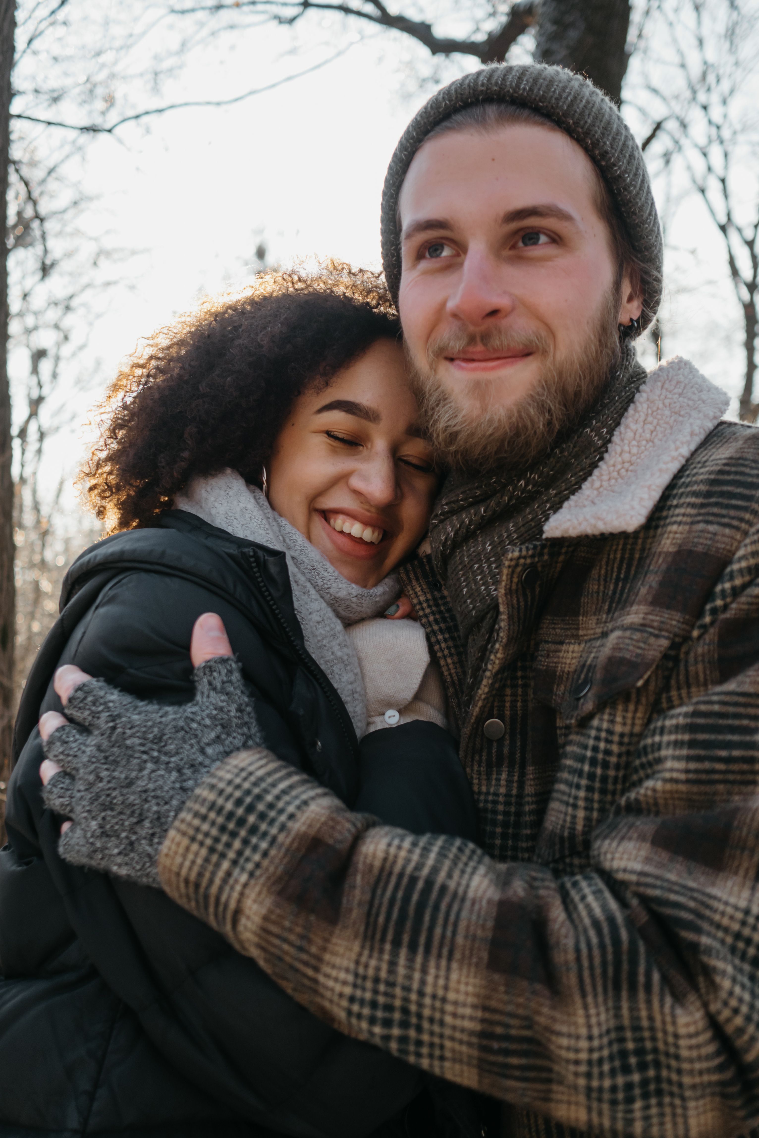 Warmly dressed couple embracing outdoors in a fall setting, exuding warmth and happiness.