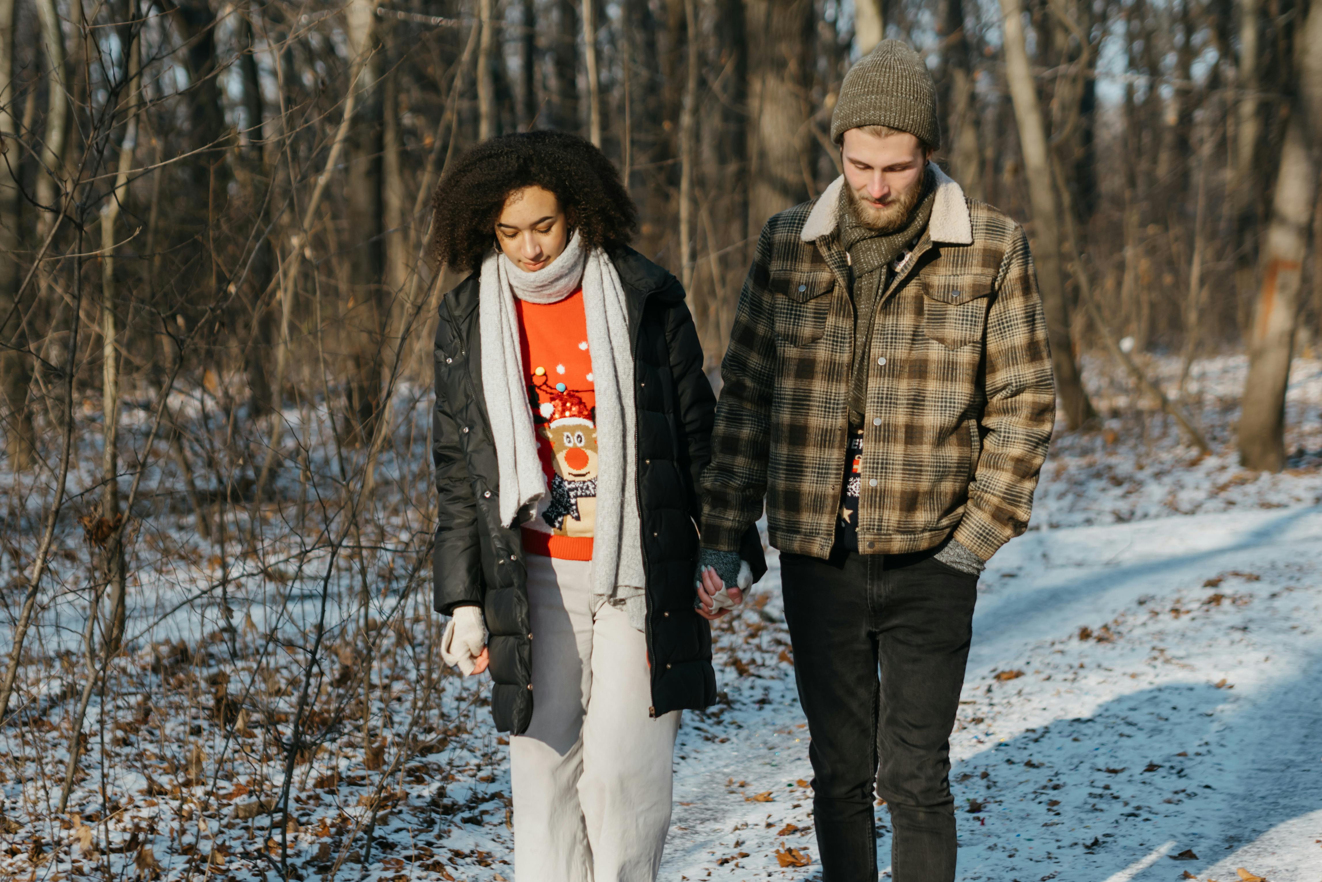 couple walking on snow covered ground near trees