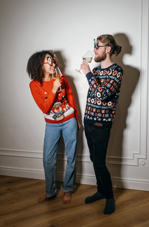 Free Joyful couple toasting in festive Christmas sweaters indoors. Stock Photo