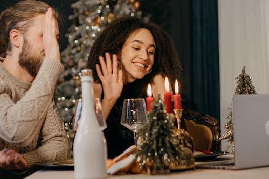 A happy couple waving during a festive video call in a Christmas-themed setting.