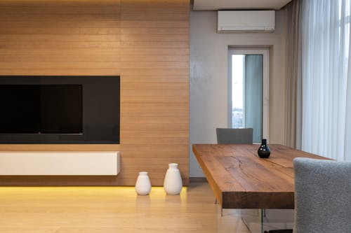 Modern TV set on wooden wall in spacious living room with table and decorated with lights and ceramic vases