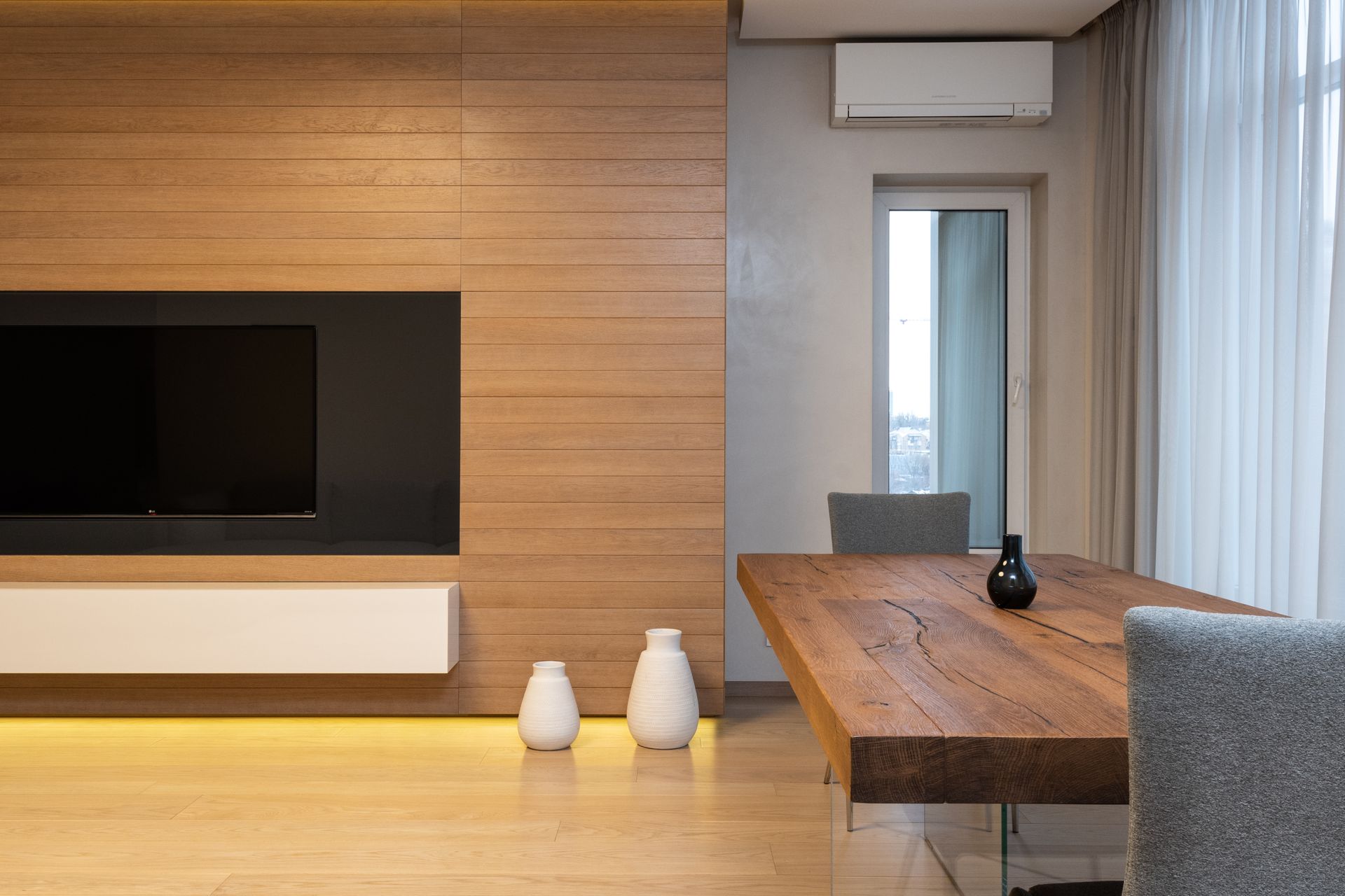 Modern TV set on wooden wall in spacious living room with table and decorated with lights and ceramic vases
