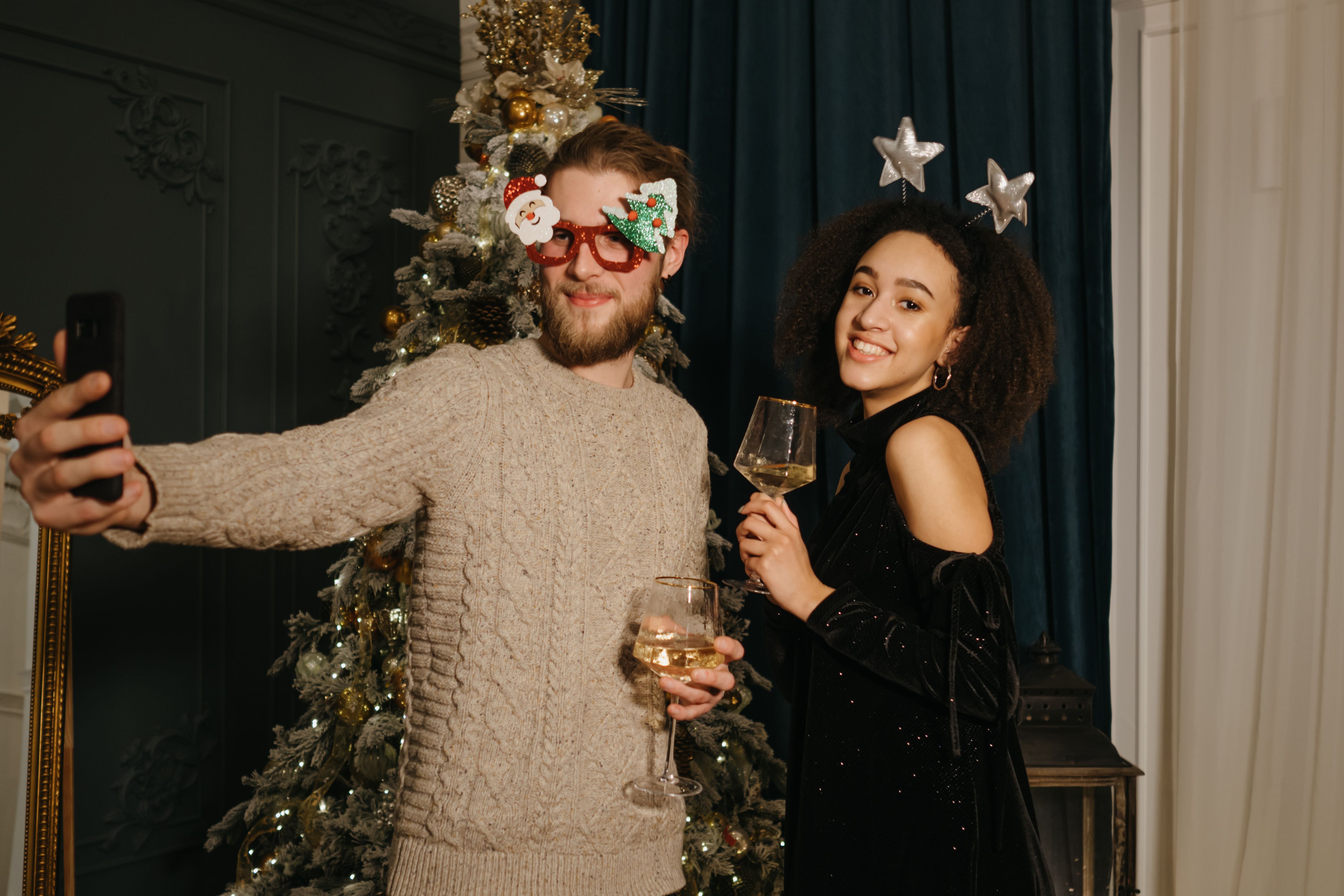 Couple celebrating Christmas with champagne and a selfie in front of a decorated tree.
