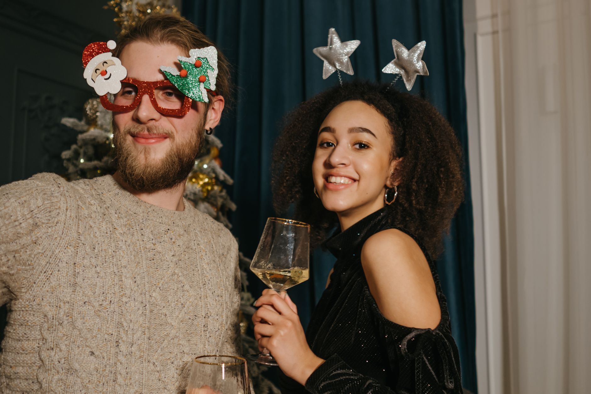 A happy couple celebrates Christmas with festive accessories and wine indoors.