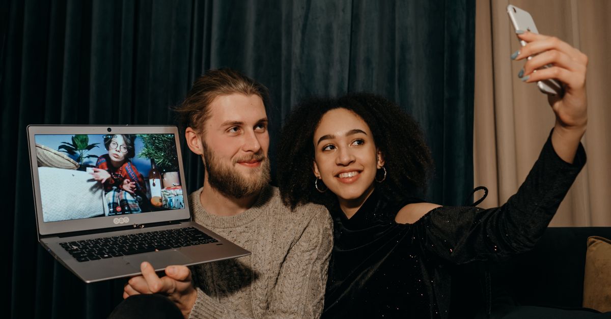 Two young people laughing while video calling on laptops in different rooms