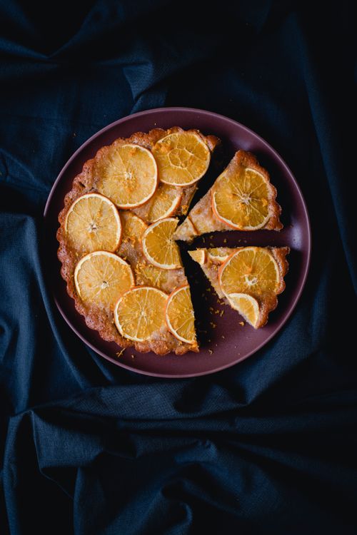 Free A delicious orange tart with slices arranged artistically on dark fabric background. Stock Photo