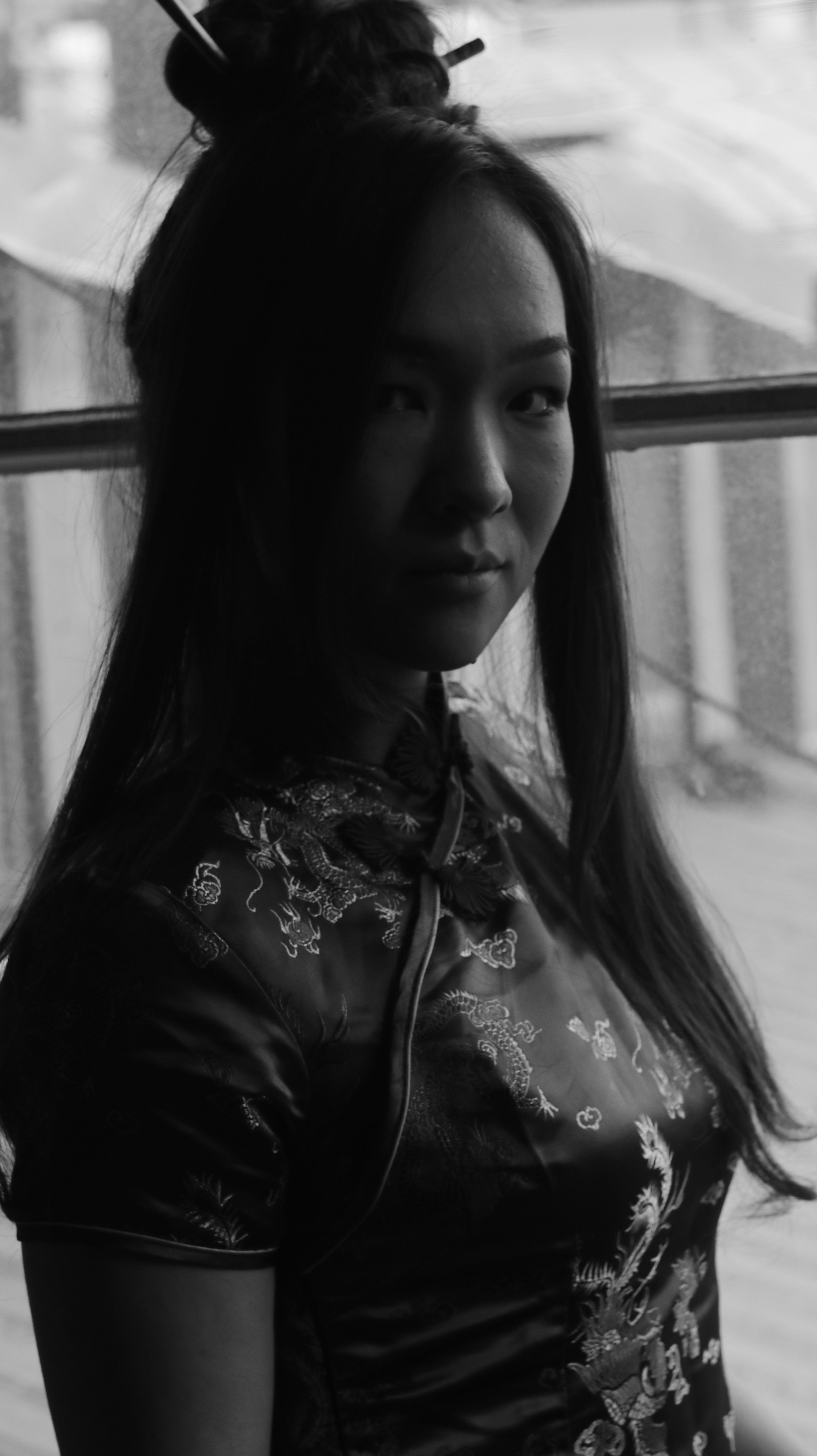 Black and white portrait of an Asian woman in traditional attire by a window.