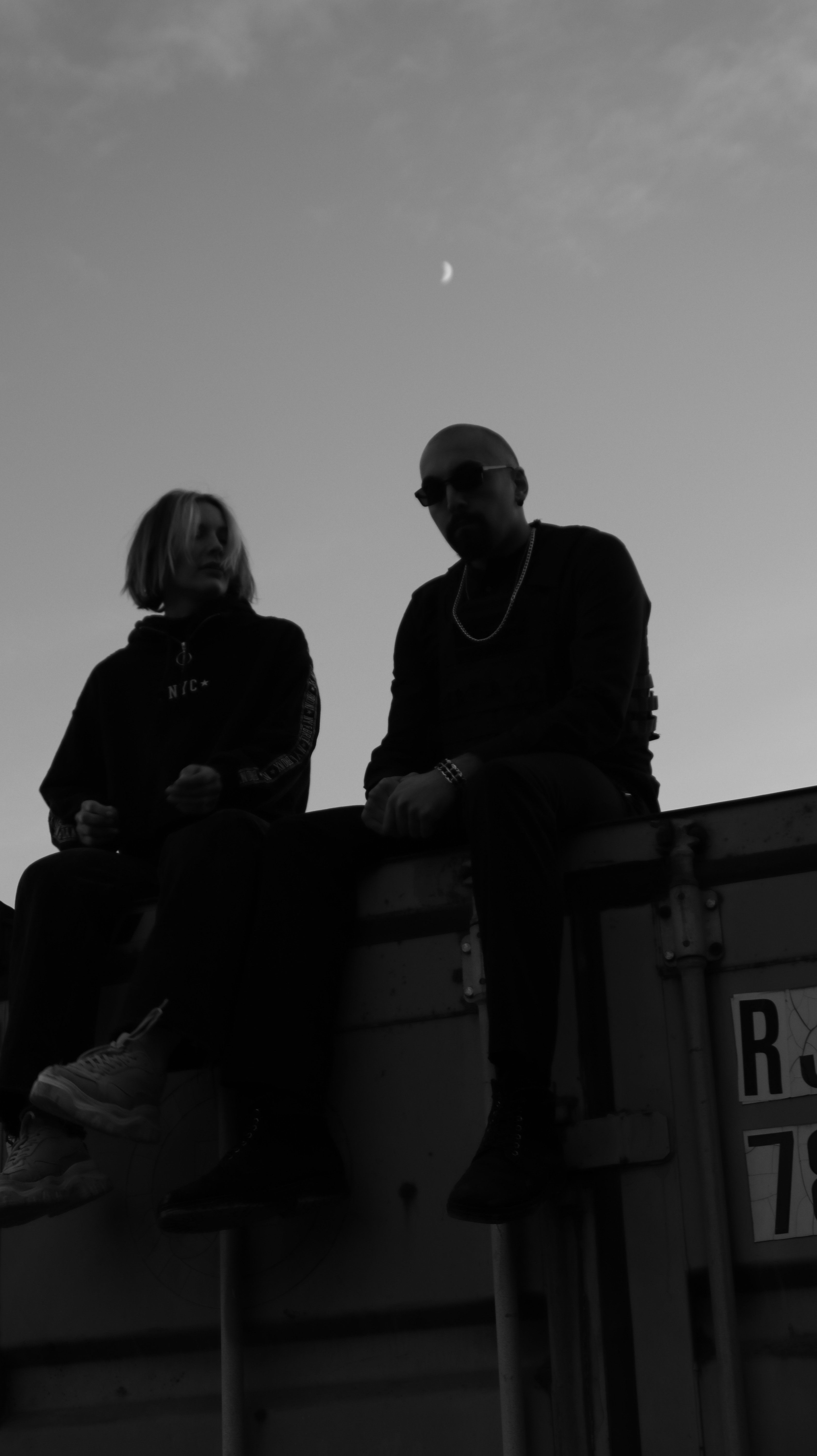 Silhouette of individuals sitting on a cargo container under a dusky sky.