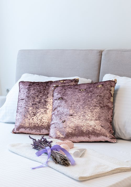 Free Cushions and bunch of lavender placed on soft bed covered with bed linens in bedroom Stock Photo