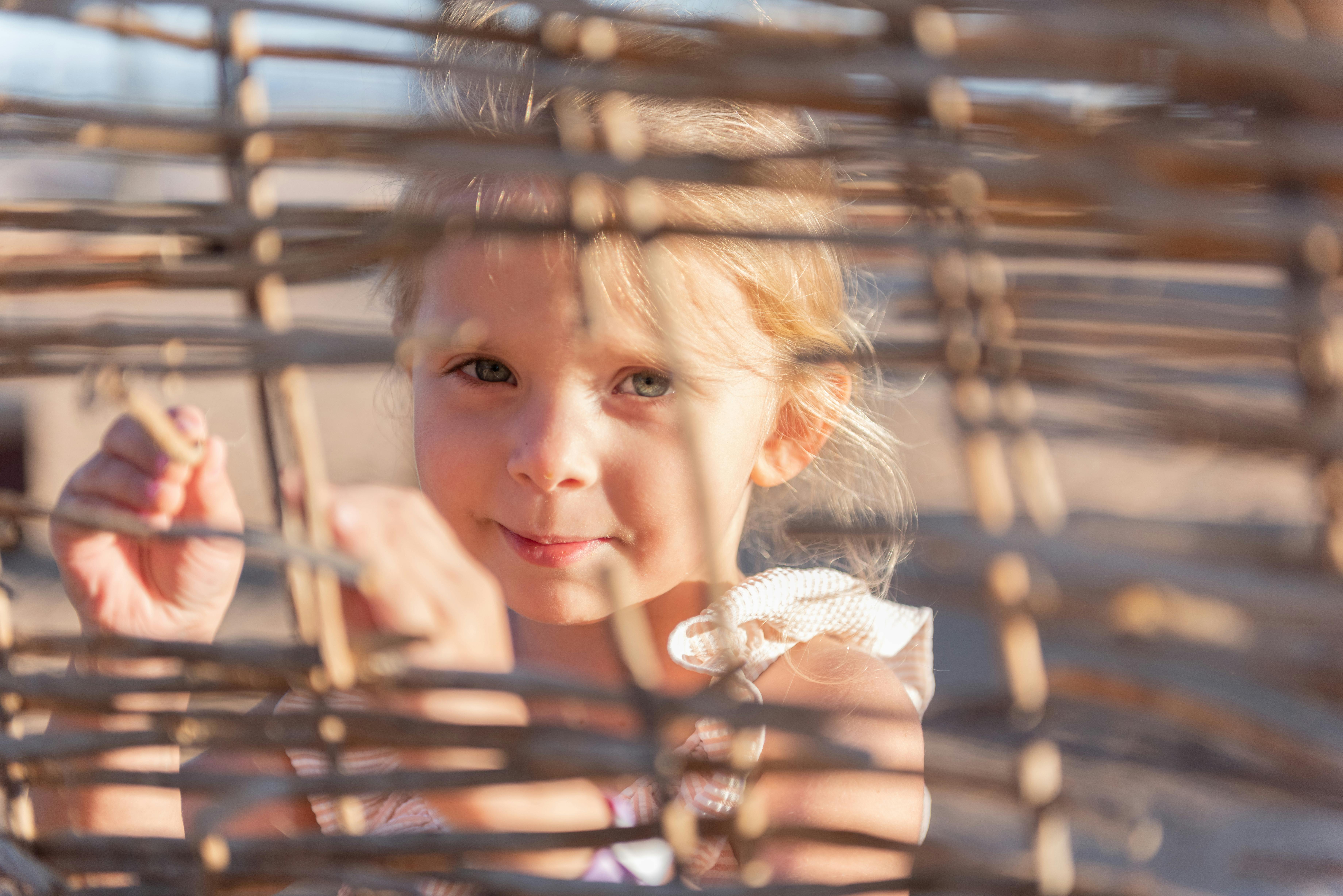 curious kid standing o sandy beach near straw fence on sunny day