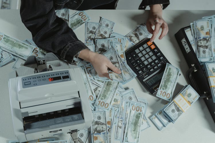 Person Holding Dollar Bills While Using A Calculator