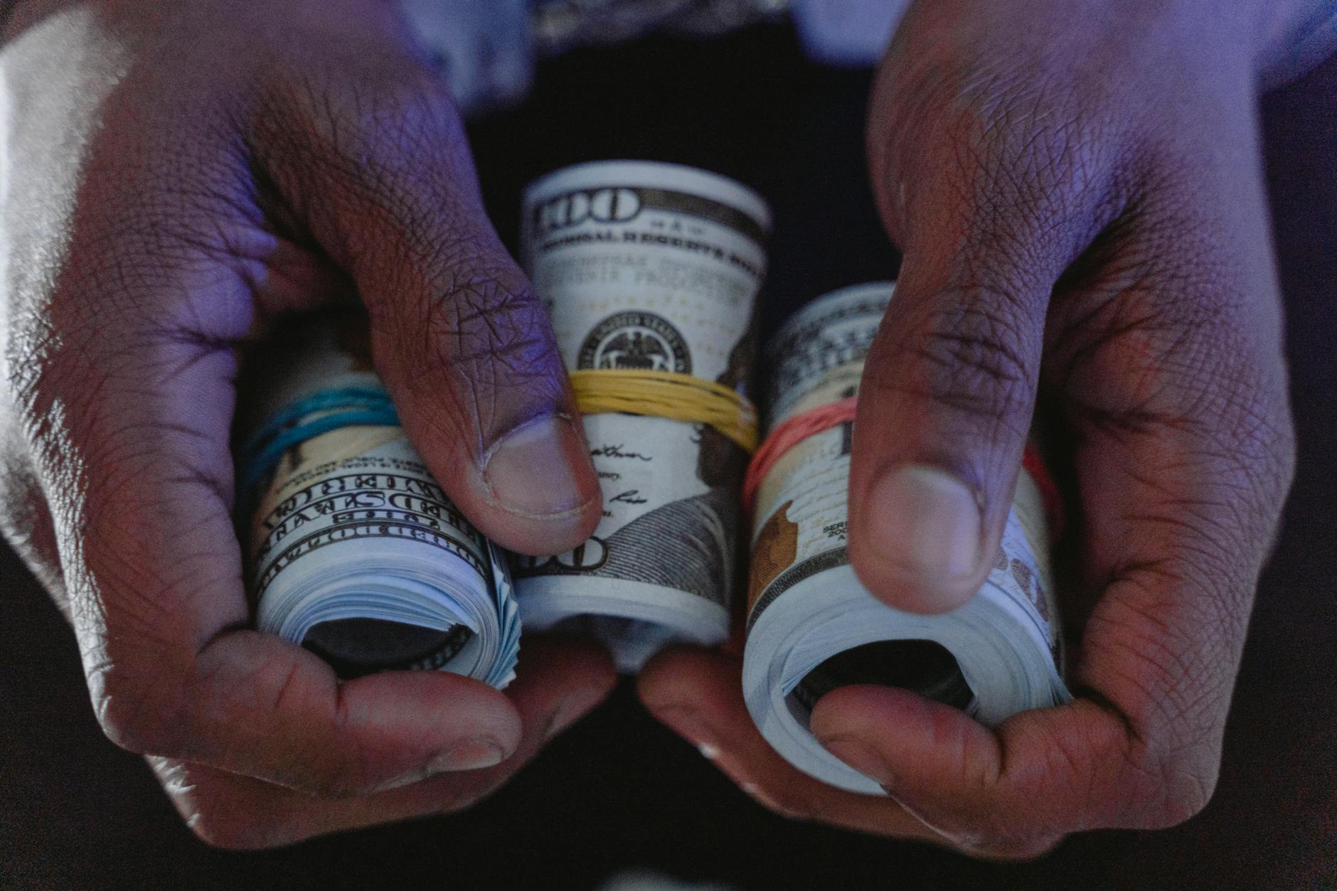 Close-up of hands holding rolls of hundred-dollar bills, symbolizing wealth and finance.