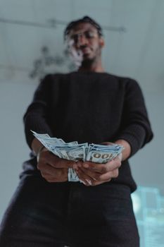 Low angle view of a man in dark clothing holding a fan of US dollar bills indoors.