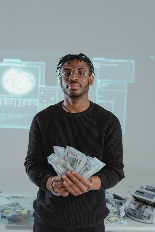 Free A man in a black sweater holds cash against a cyber-themed backdrop with screens. Stock Photo