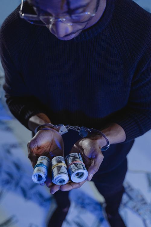 Free A man in handcuffs holding rolled US dollar bills, symbolizing cyber fraud or theft. Stock Photo