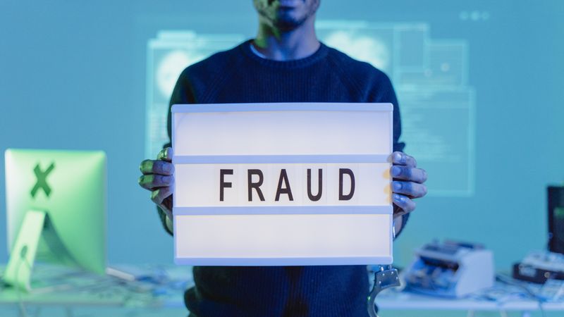 A man holding a sign reading 'FRAUD' in a tech environment, highlighting cybersecurity concerns.