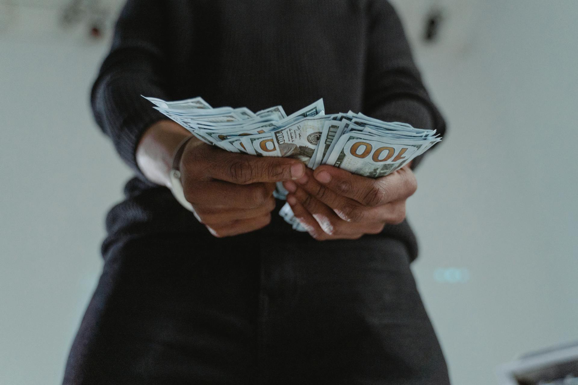 A close-up view of a person holding a stack of US hundred dollar bills indoors.