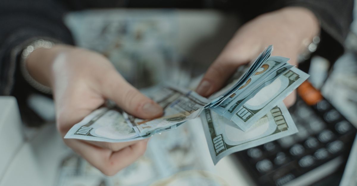 Close-up of hands counting hundred dollar bills with a calculator in the background.