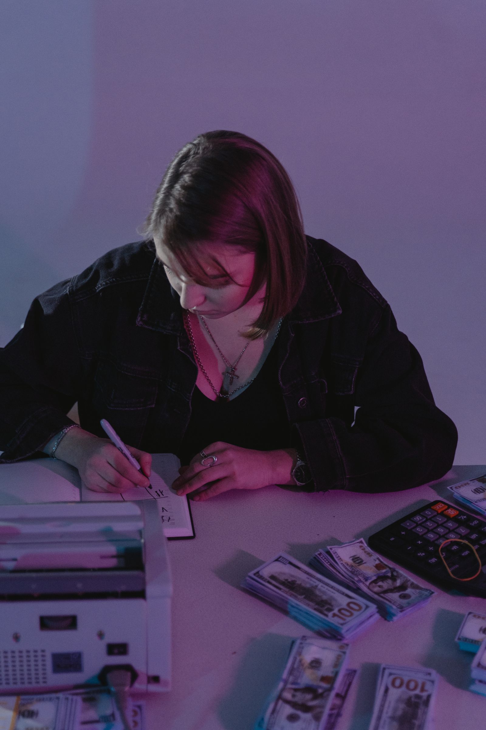 A woman writing notes beside cash and a calculator.