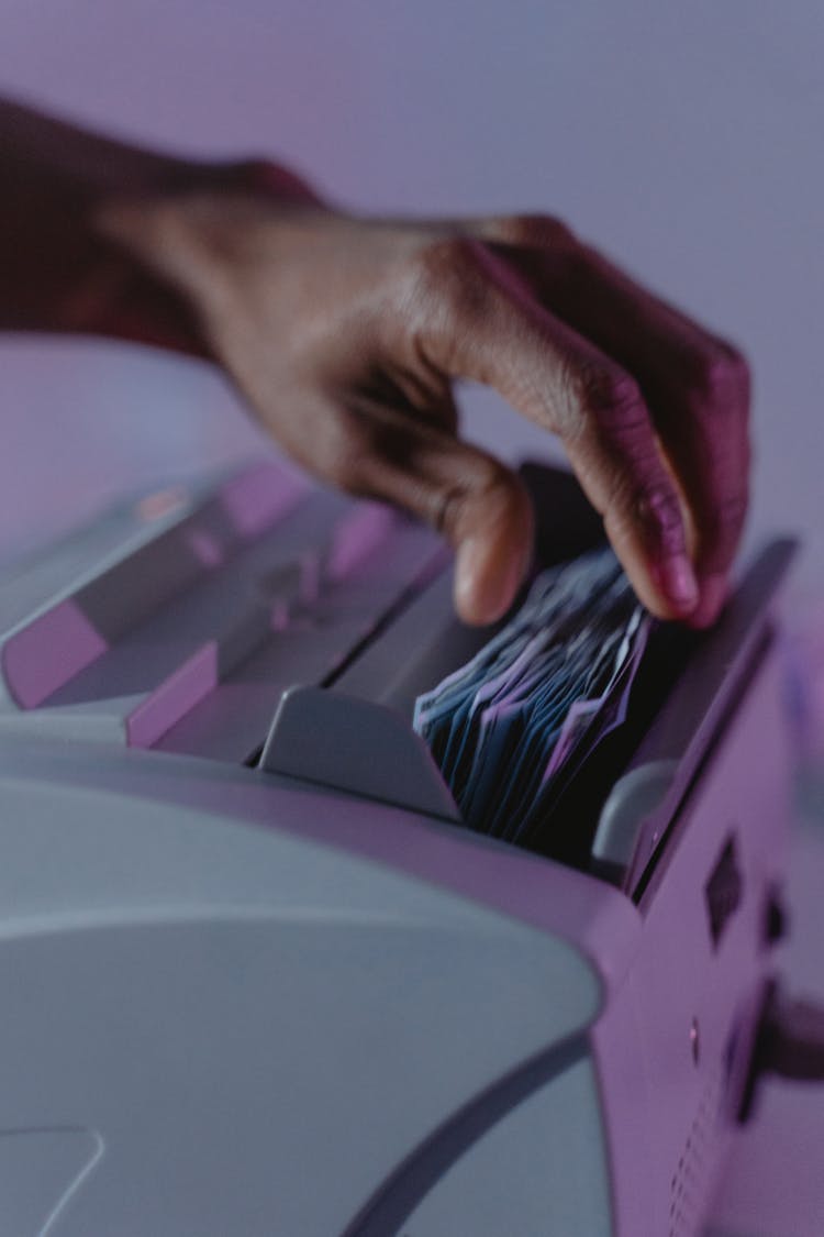 A Person Getting Money Bills From A Money Counter