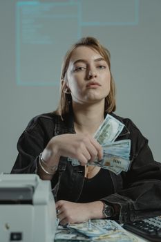 A confident woman in black denim holding cash at her desk in a modern office.