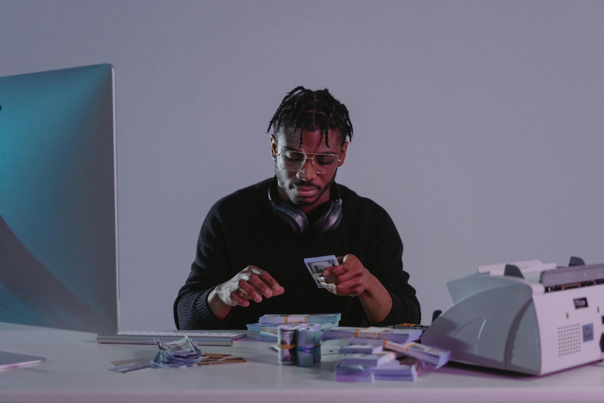 Focused man counting cash at an office desk with a computer and cash counting machine.