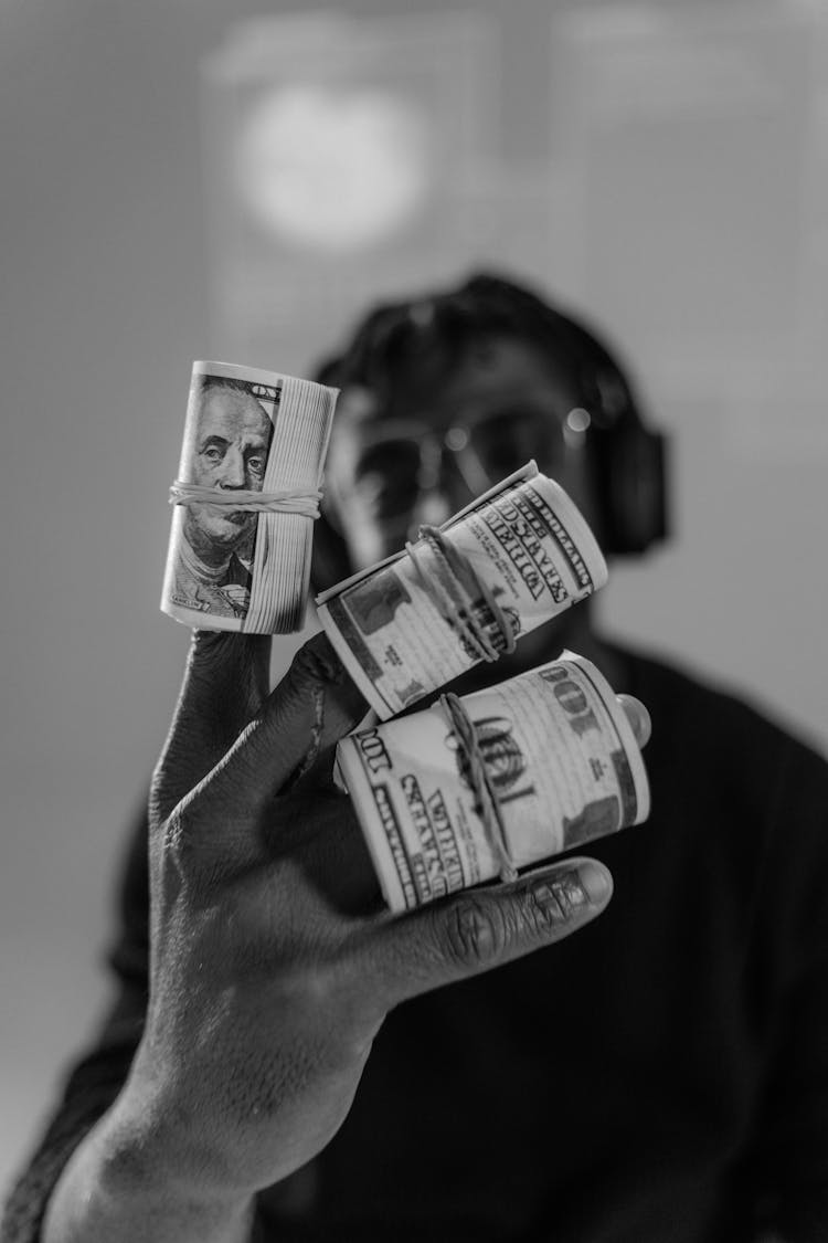 Grayscale Photograph Of Rolls Of Money On A Person's Fingers