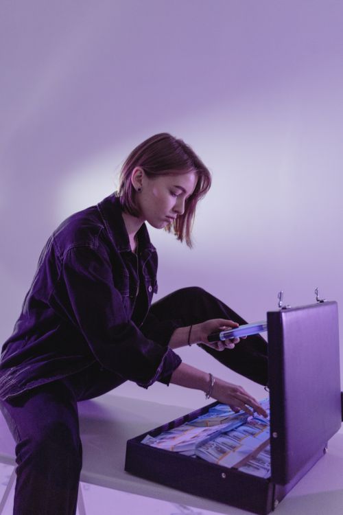 Free A young woman counts cash in a briefcase under purple lighting, suggesting business or finance themes. Stock Photo