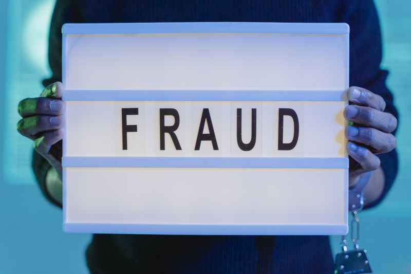 Close-up of hands holding a sign with fraud, illuminated in blue light
