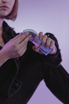 Close-up of a woman counting cash with a purple hue background, wearing a jean jacket.