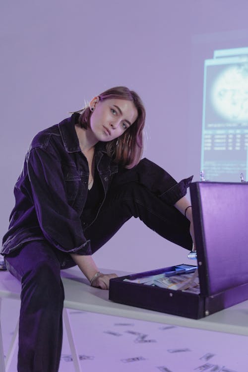 Woman Sitting on a Table in front of a Briefcase Full of Money