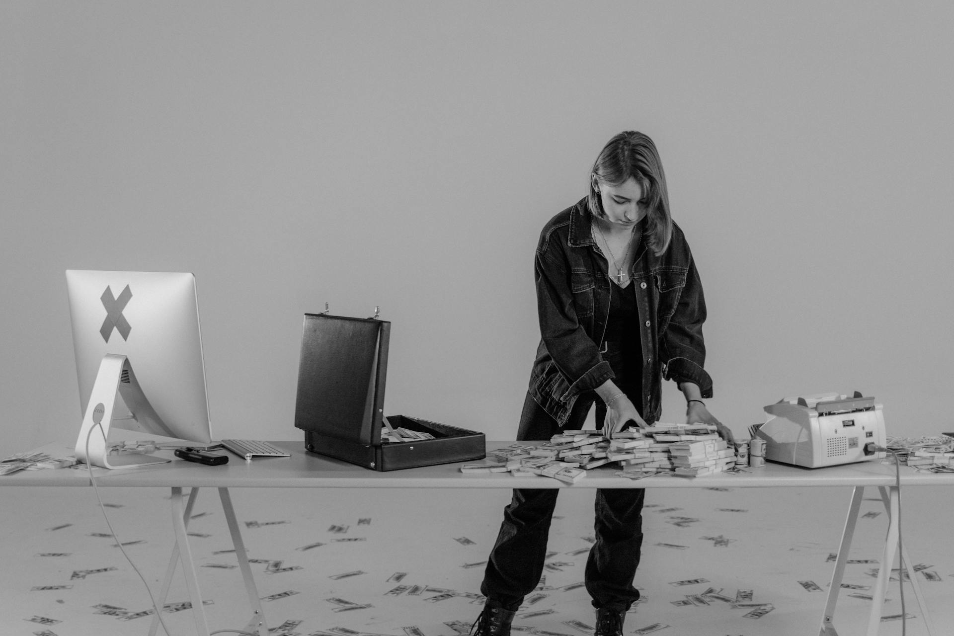 A woman arranges stacks of money on a table with a briefcase and computer.