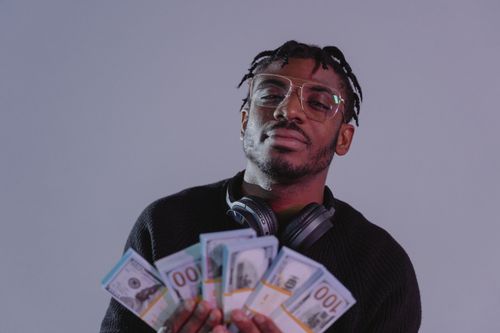 Free Portrait of a man holding bundles of cash wearing glasses and headphones. Indoor setting. Stock Photo