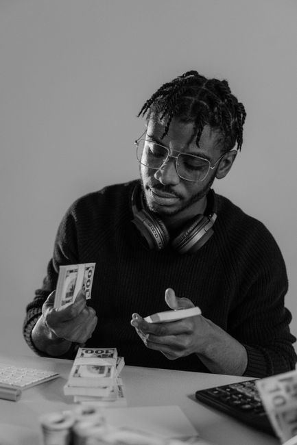 Black man sitting indoors calculating and counting money with focus and headphones. Black man sitting indoors calculating and counting money with focus and headphones.