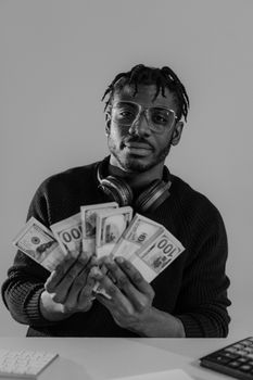 A black and white photo of an adult male holding US dollars, wearing headphones and glasses.