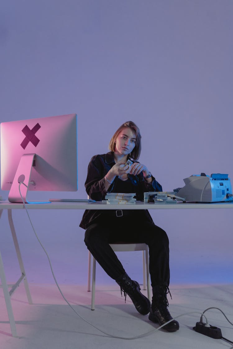 Woman In Black Jacket Sitting In Front Of A Pile Of Money 