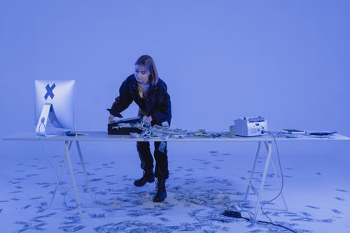 Free A young woman standing at a desk filled with money, suggesting cyber crime or financial scam. Stock Photo