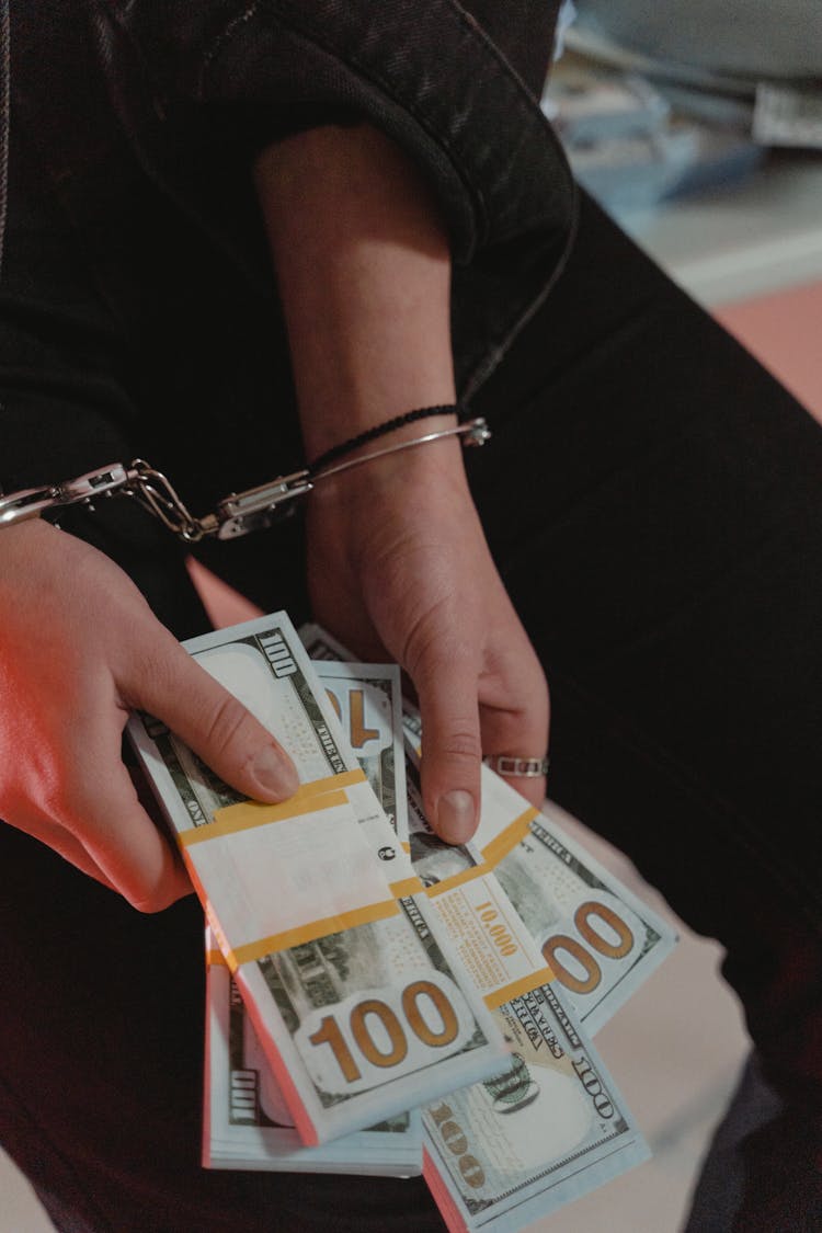 Person In Handcuffs Holding Bundles Of Cash