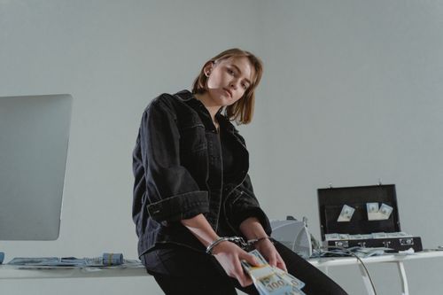 Free Young woman in black jacket handcuffed with cash, conceptual indoors setting. Stock Photo