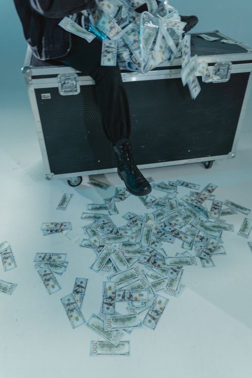 Free Model sitting on road case with cash spilling out, creating a dramatic money scene. Stock Photo