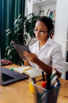 Young black woman with headphones studying using a digital tablet indoors.