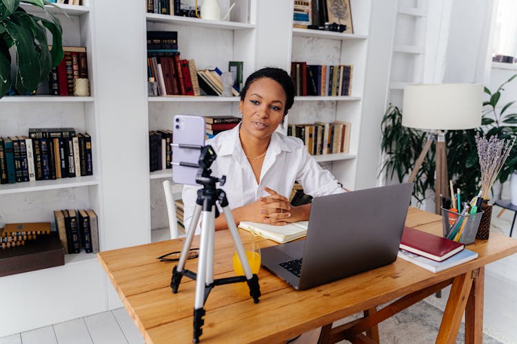 Woman In White Shirt Sitting At Desk With Silver Laptop And Smartphone