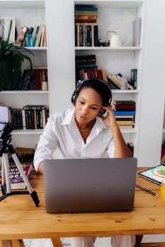 Woman wearing headphones using a laptop at a desk in a home office setting.