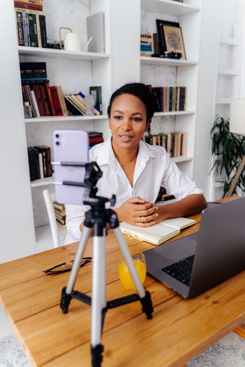 Free A woman using a smartphone and laptop for a video call in a modern home office setting. Stock Photo